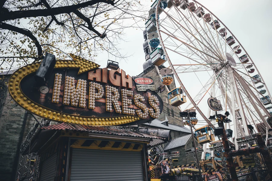 Riesenrad und beleuchtete Fahrgeschäft-Aufschrift zwischen kahlen Ästen