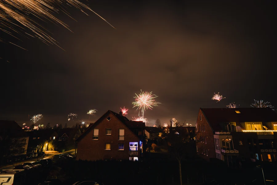 Feuerwerk zeichnet helle Spuren über dunklen Dächern