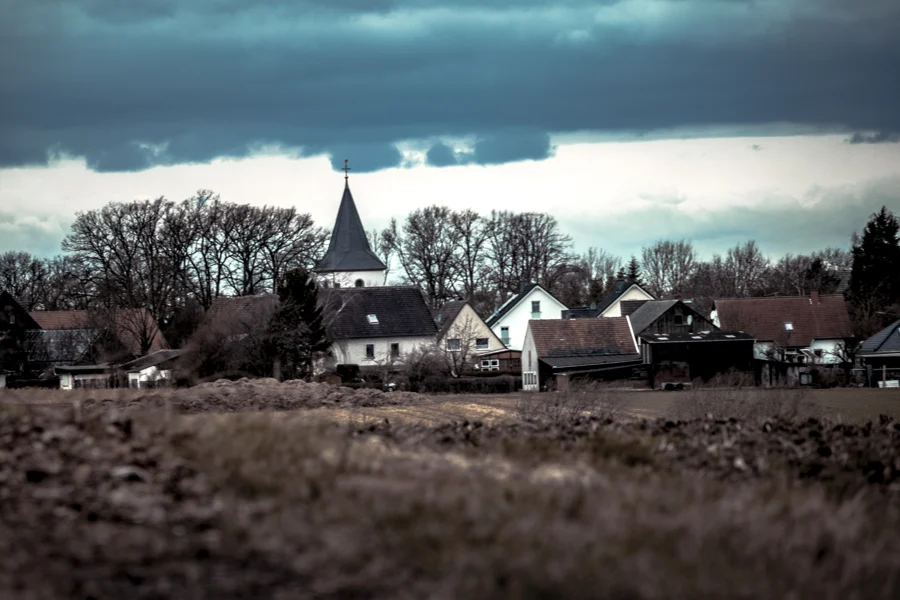 Ein dunkles Feld vor Häusern und einem Kirchturm unter schweren Wolken