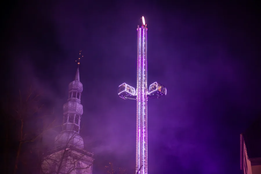 Violett beleuchteter Freifallturm neben Soester Kirchtürmen