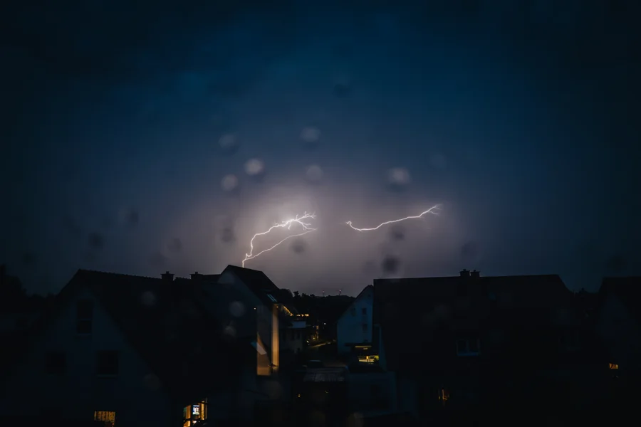 Blitze in einem dunklen Nachthimmel über Häuserdächern